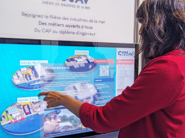 Totem tactile en inox personnalisé aux couleurs et logo de CInav, et diffusant de la vidéo sur un grand écran afin de faire la promotion des métiers d