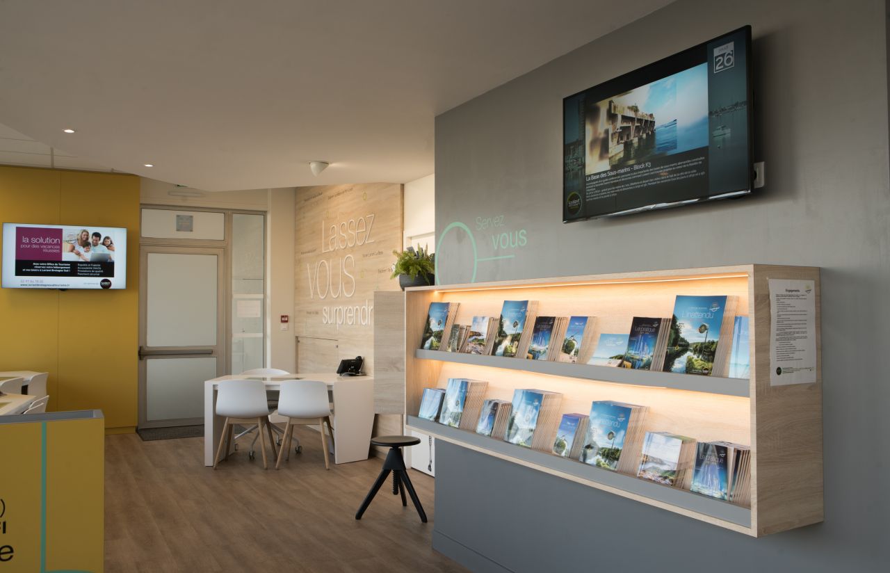 Dans un Office de Tourisme, un écran d'affichage dynamique surplombe les brochures papier
